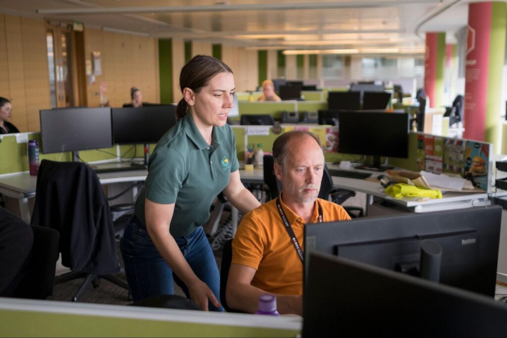An ergonomics consultant observing a worker at a desk in a modern office.