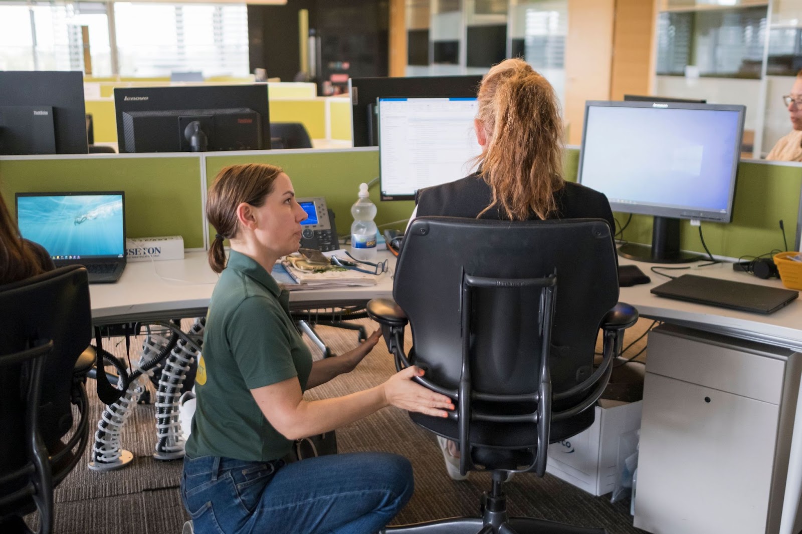 Person demonstrating proper posture at an ergonomic office design workstation, showing chair, desk, and monitor setup.