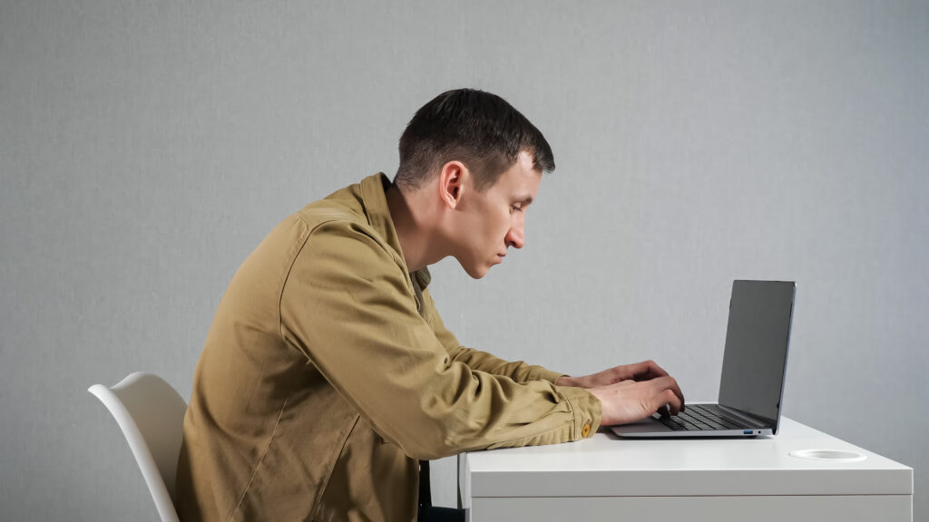 Person hunched over a laptop, showing signs of bad desk ergonomics.