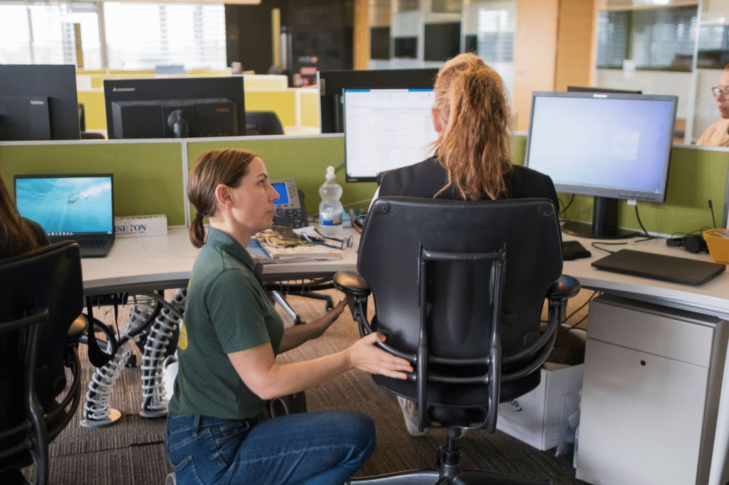 A consultant teaching an employee how to adjust their chair.