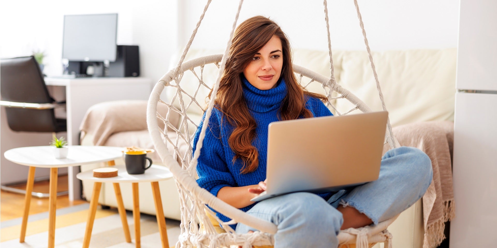 A woman sitting in a hammock, working on her laptop