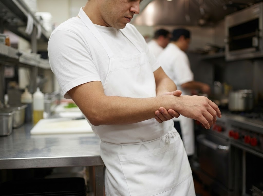 Tired chef rubbing strained wrist in busy kitchen