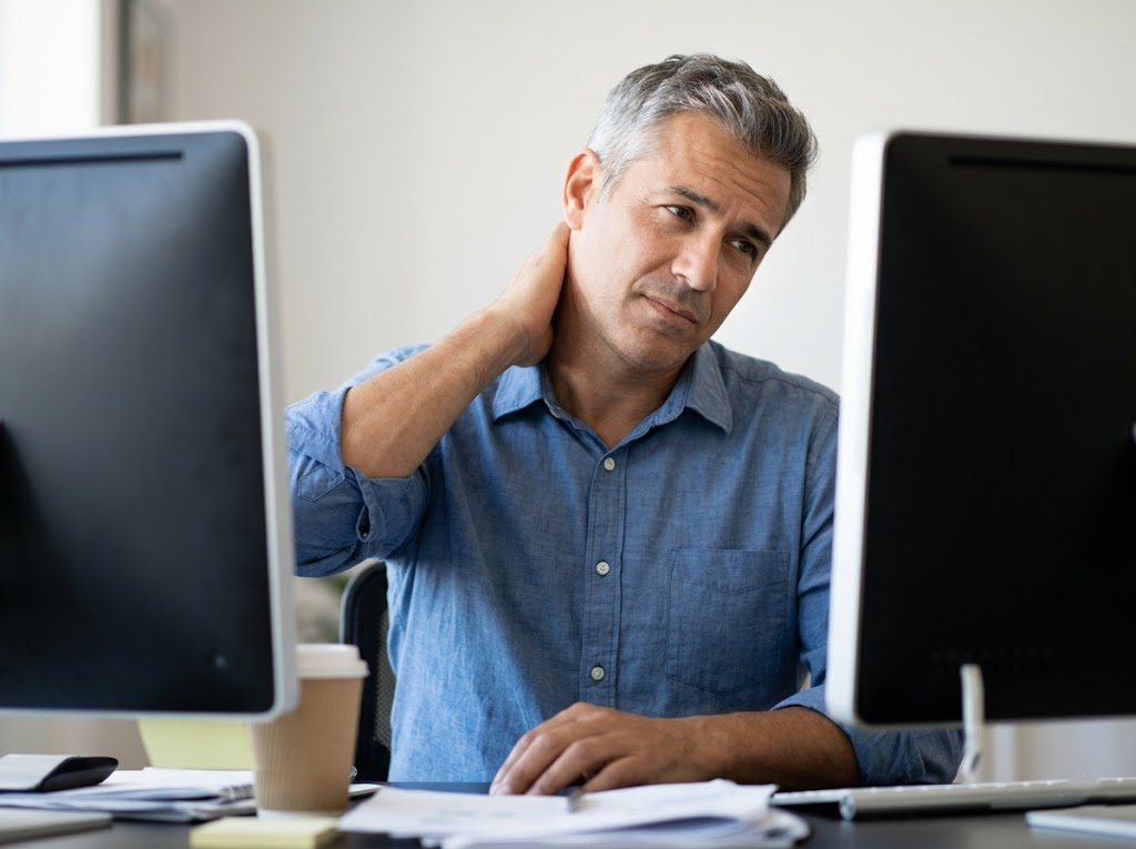  Man gently rubbing his neck between dual screens. 